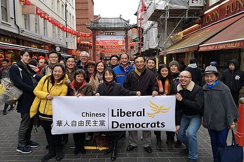 Group of Chinese LibDems smiling in front of London Chinatown gates with Chinese Lib Dem banner